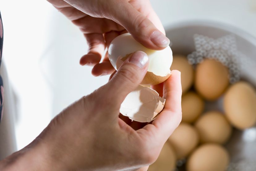 A woman peels a boiled egg.