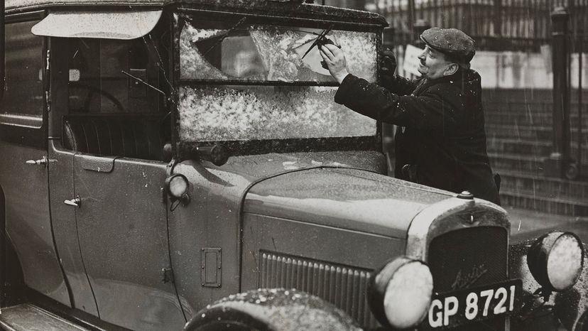 man cleaning snow off car windshield in February 1938