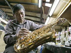 Asian man building a saxophone in a factory.