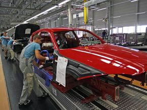 Employees work on a red vehicle in an assembly line at a BMW factory.