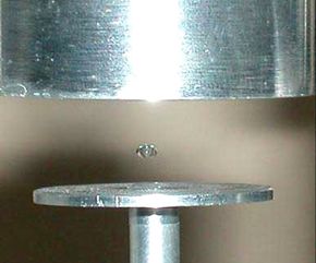 A drop of liquid floats above a metal disc.