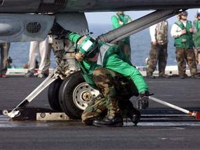 A member of the USS George Washington flight-deck crew checks an F-14 Tomcat's catapult attachment.