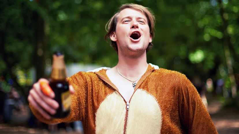 A drunk guy wearing a bear onesie and holding a bottle of beer.