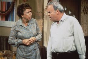 Characters from the TV show 'All in the Family' look at one another.