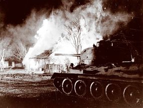 A Russian T-34 tank rolls through a burning village during the battle of Kursk in July 1943.