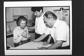 Shirley Gold, who has Alzheimer's, concentrates on taking a drink from a glass of water as her son and husband look on.