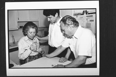 Shirley Gold, who has Alzheimer's, concentrates on taking a drink from a glass of water as her son and husband look on.