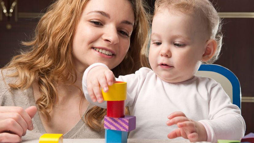 A mother helps her daughter build a tower with blocks.