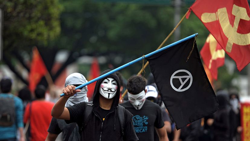 A man wearing a Guy Fawkes mask flies an anarchy flag as he takes part in a May Day demonstration for workers' rights in El Salvador in 2012. Many anarchists have adopted the Guy Fawkes mask, made famous in the graphic novel 'V is for Vendetta.' Jose CABEZAS/AFP/Getty Images