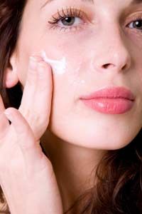 Woman applying moisturizer to face.