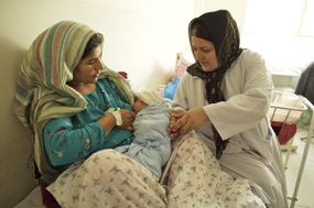 woman holding baby breastfeeding with doctor accompanying