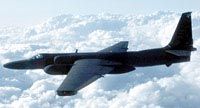 A&nbsp;U-2 spy plane flying, against a background of fluffy white clouds.