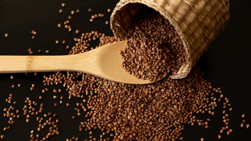 Buckwheat seeds in wooden spoon on a brown wooden table.