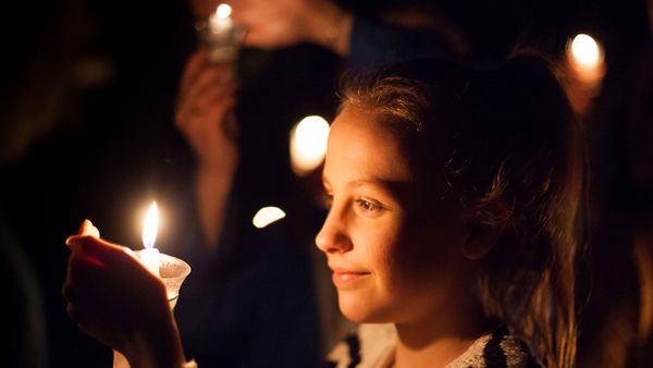 Women gather around a candle in the night, illuminated by its flame.