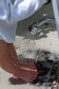 An outdoor shower being used to rinse sand off of someone's feet.&nbsp;