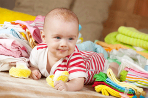 A baby smiling on the floor surrounded by clothes and towels.