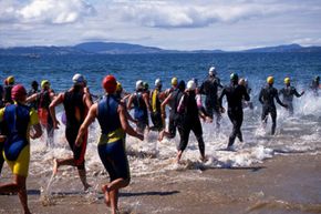 Triathletes in wetsuits head into the water, beginning the most dangerous leg of the race.