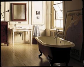 A traditional claw-foot tub and pedestal sink share space with a loft-type window and a modern lamp.