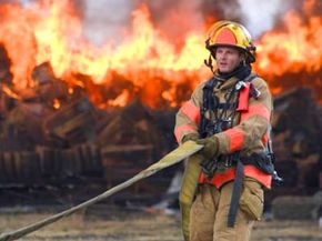 A firefighter pulling a hose to get ready to fight a warehouse blaze.