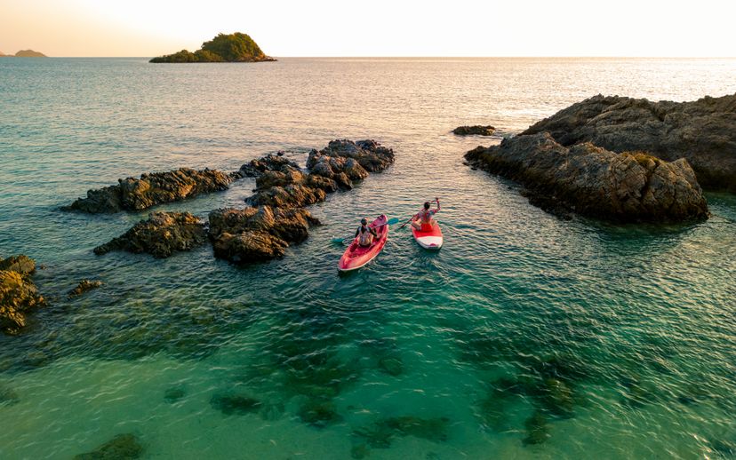 Aerial view - Asian two women enjoy the water aqua sport on the seaside. Relaxing on kayak and paddle board at emerald crystal clear sea. Summertime, Weekend holidays. Thailand. Aerial drone photo.