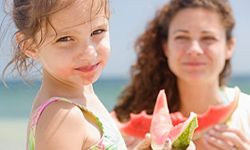 Mother and daughter eating watermelon at the beach. 