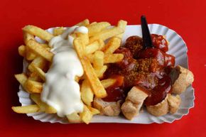A traditional German currywurst, accompanied by french fries with mayonnaise, is served on a paper plate in the Prenzlauer Berg district of Berlin.