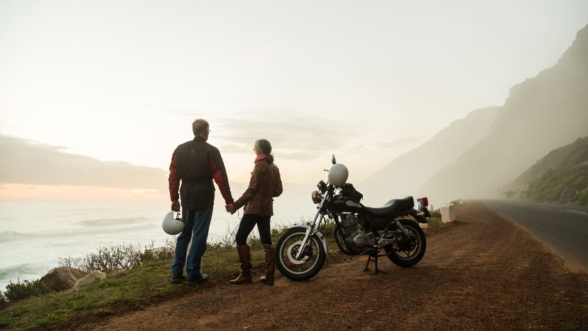 A man and woman standing at the edge of a cliff with their motorcycle parked behind them. 