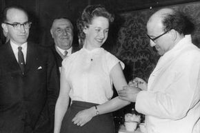 Dr Jonas Edward Salk (L), who developed the first vaccine against poliomyelitis, looks on as Dr J V Acius-Ferante vaccinates a woman.