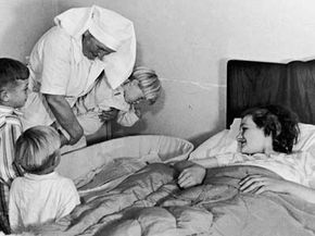 Three boys are introduced to their newborn baby sister by the midwife after a home delivery, August 1946.