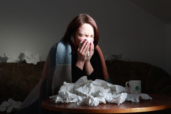 Woman blowing nose at table