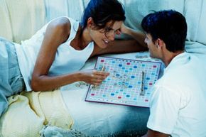 A couple playing Scrabble on a couch.
