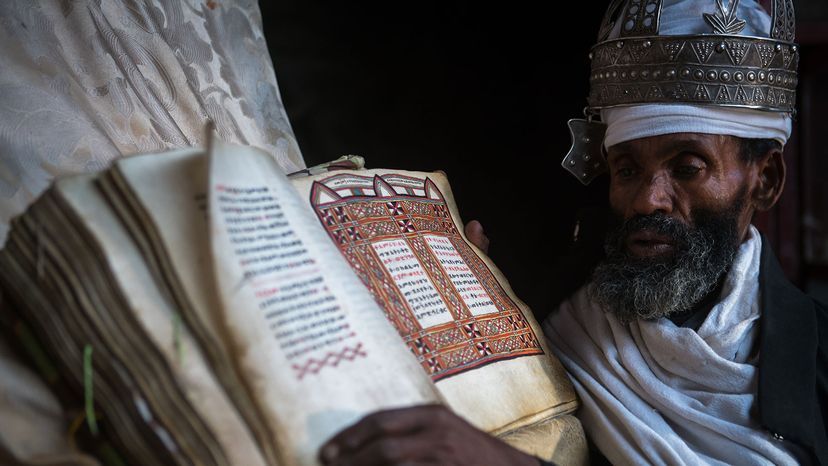 Ethiopian Orthodox priest shows an ancient Bible“width=