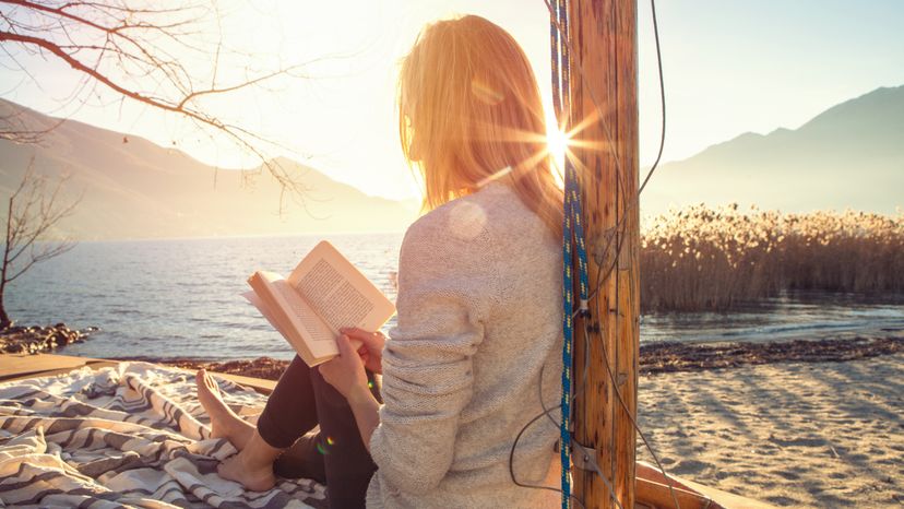 A young woman sitting by a lake, reading a book. 