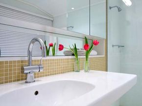 Porcelain sink in an off-white bathroom with two pink flowers in a vase.