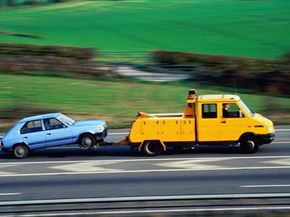 Yellow truck towing a blue car on the highway.