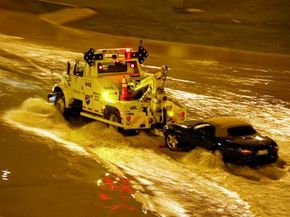 Tow truck towing a convertible out of a flooded roadway.