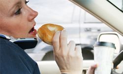 woman driving while talking on the phone and eating breakfast