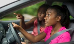 Teenager and mother behind wheel of car. 