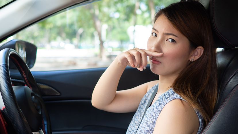 Young woman holding her nose because of bad smell in car