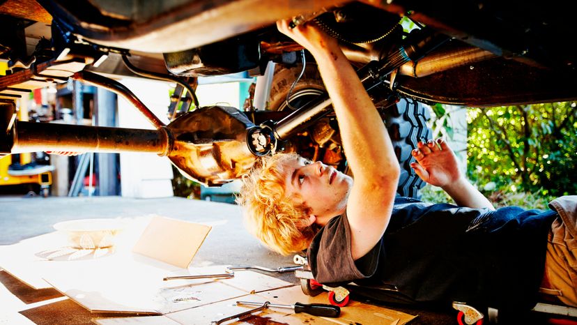 Teenage boy lying on driveway outside of garage replacing oil pan of off road vehicle