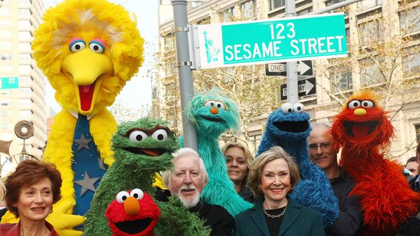 Puppeteer Caroll Spinney, Sesame Street co-founder and TV producer Joan Ganz Cooney, and Sesame Street cast members pose under a '123 Sesame Street' sign 