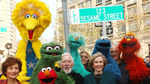 Puppeteer Caroll Spinney, Sesame Street co-founder and TV producer Joan Ganz Cooney, and Sesame Street cast members pose under a '123 Sesame Street' sign