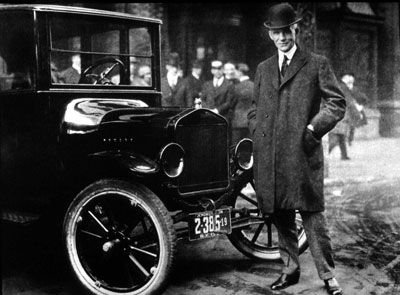 Henry Ford stands next to the Model T.