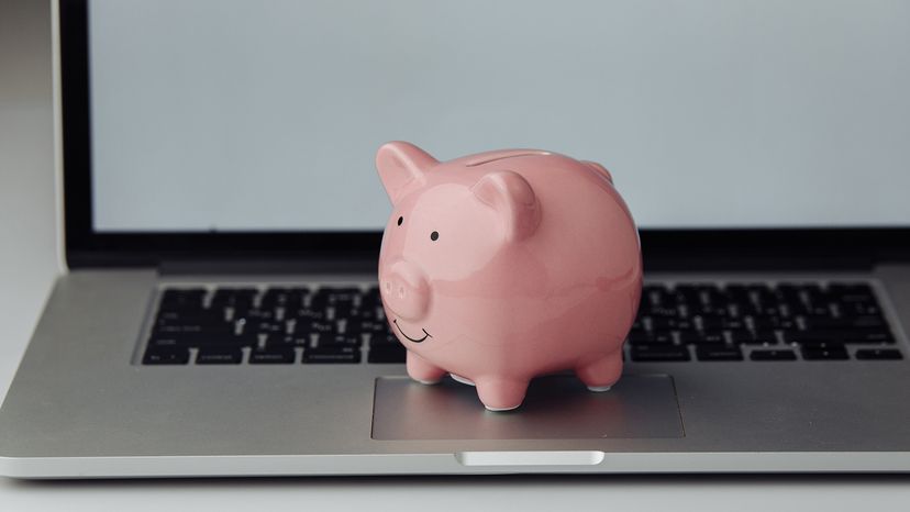 Pink piggy bank on silver Mac laptop with black keys and a white screen