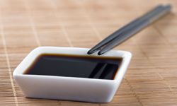 &nbsp;A small while bowl of soy sauce with two chopsticks leaning on it sits on a bamboo mat.