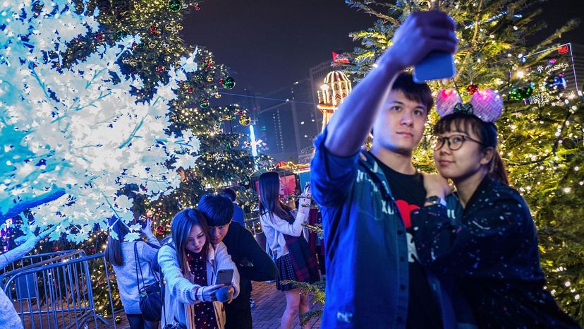 Young people take pictures in front of Christmas trees.