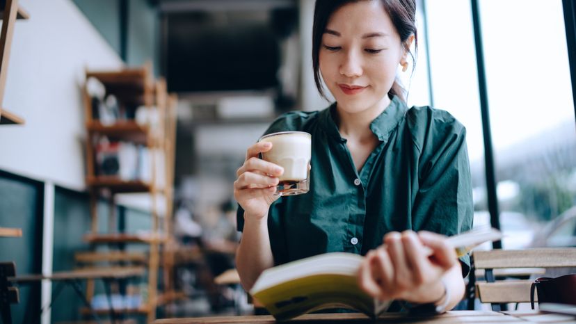 Young woman taking a break, having a quiet time enjoying a cup of coffee, and reading a book in a cafe