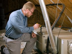 Service man kneels beside a furnace in a home attic, to inspect it for before winter usage.