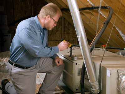 Service man kneels beside a furnace in a home attic, to inspect it for before winter usage.