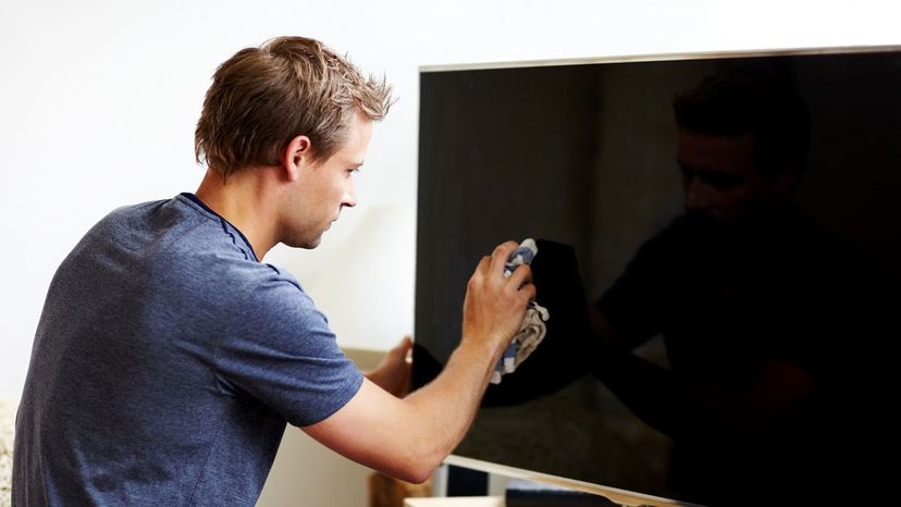 Man cleaning a flat screen TV with a rag.